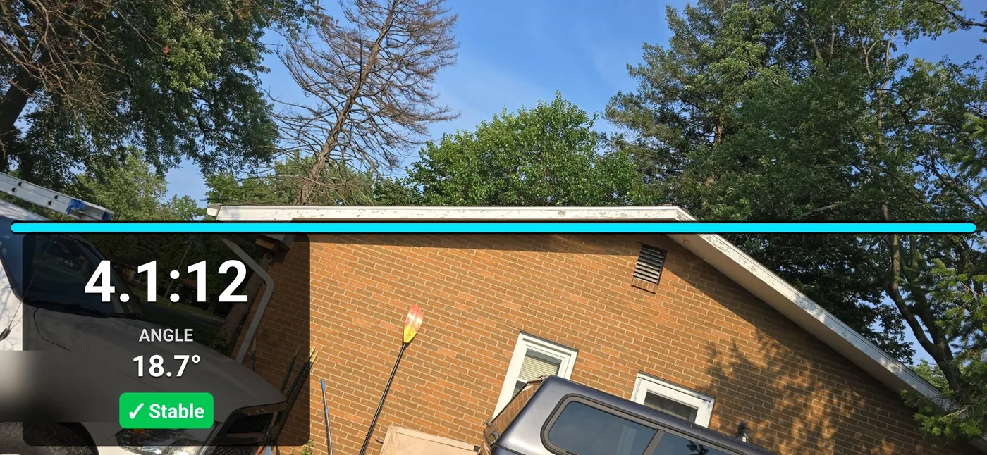 Pitch Please Camera Mode measuring a low-slope brick house roofline from the ground, reading 4.1:12 pitch at an 18.7 degree angle with the cyan alignment line on the fascia and a stable indicator